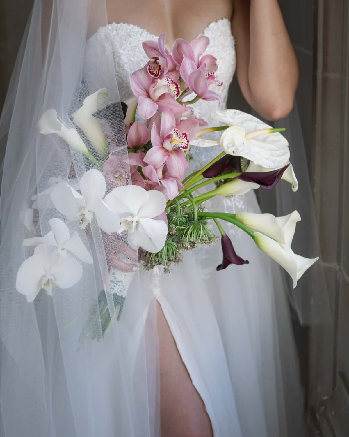 Bridal bouquet with pink cymbidium orchids, white phalaenopsis, burgundy callas, framed through a veil